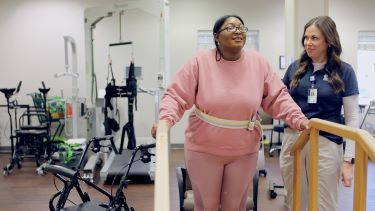 A therapist steadies Alexis Prue as she takes a few steps with support at Tidelands Health Neurological Rehabilitation Center.