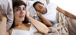 A woman holds a pillow over her ears to ignore her husband's snoring