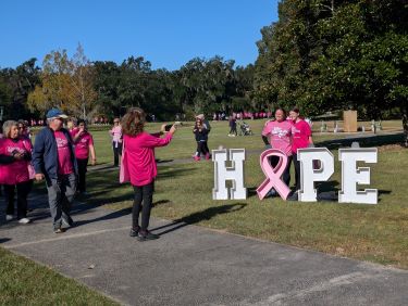 Participants in the Tidelands Health In the Pink breast cancer awareness walk at Brookgreen Gardens pose for a photo behind white letters spelling "hope."