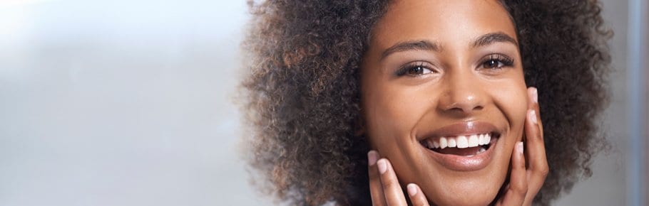 A woman smiles while holding her face.