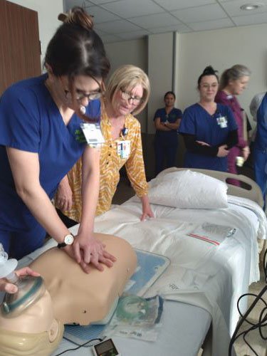 A nursing student practices CPR on a manikin with a Tidelands Health CPR instructor overseeing.