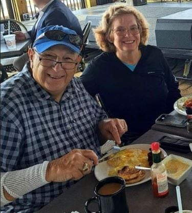 Jack Simcsak, wearing a ball cap and a big smile, sitting with his wife at a table at Dead Dog Saloon.