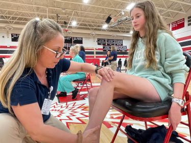 Tidelands Health physical therapist Camila Denshuick kneels as she checks the leg movement of 13-year-old Avery Fleming during free sports physicals offered by the health system in the gym at Waccamaw High School.