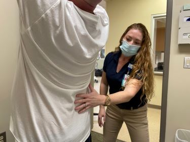 A physical therapist checks the back of a patient with his arms raised over his head.