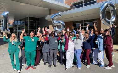 A group of health care professionals celebrate with hands raised holding balloons for "150" representing Tidelands Health being named one of the top 150 places to work in health care.