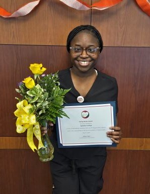 Tyeishia Cochran poses with her Caring Hearts certificate and a vase with yellow roses.