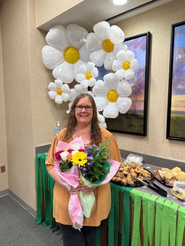 Daisy award winner nurse Jeanette Padgett holds flowers standing in front of daisy-shaped balloons.