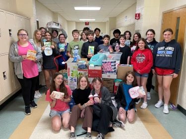 About 20 Junior Beta Club members at St. James Middle School pose in the school's hallway with baby supplies they donated to Tidelands Health Pediatrics.